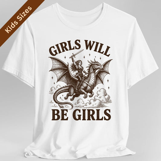 White kids t-shirt. The design reads Girls Will arched across the top and Be Girls across the bottom in chunky distressed capitals. In between, a woman adventurer in leather armor with long flowing hair rides a large winged dragon through the clouds, holding a sword raised high above her head. Dark brown woodcut lines with small stars scattered around.
