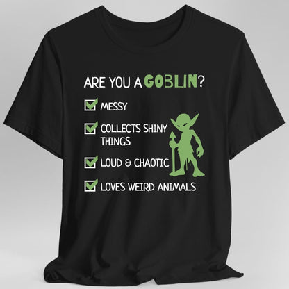 Black t-shirt. Reads "Are you a goblin?" across the top, with "goblin" picked out in green. Below, four ticked checkboxes list "Messy", "Collects shiny things", "Loud and chaotic" and "Loves weird animals". A small green goblin stands to the right of the list.