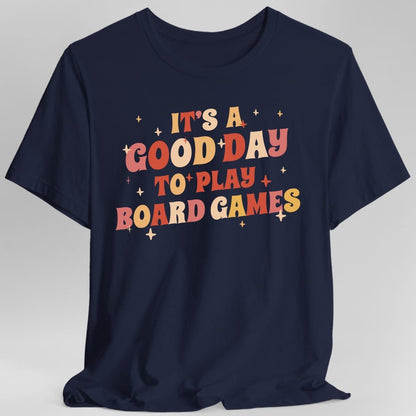 The same Good Day to Play Board Games, groovy design, on a navy t-shirt.