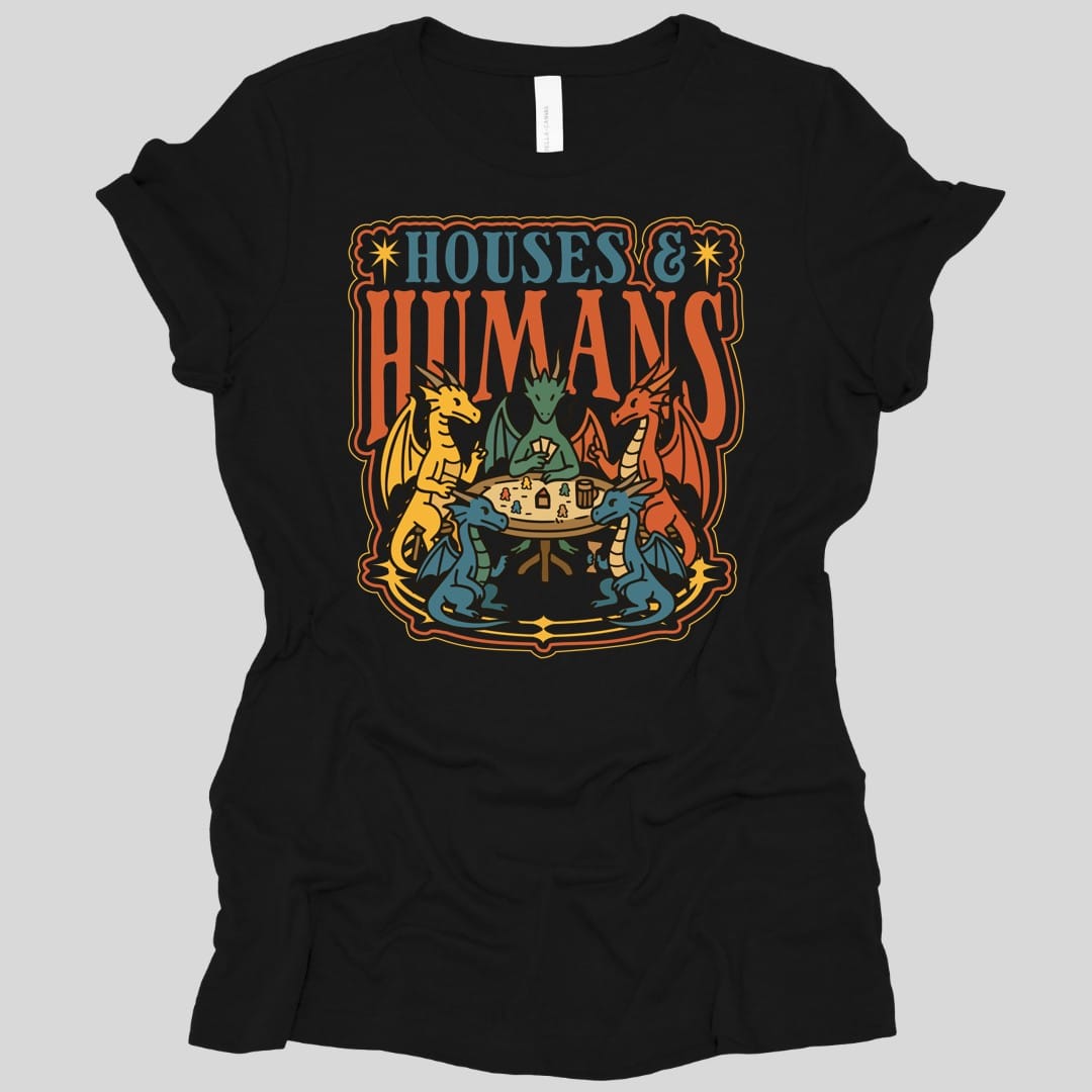 Black women's t-shirt. The design reads "Houses &" in blue serif capitals and "Humans" in tall orange capitals beneath it. Below the words five dragons in yellow, green, red and blue sit around a round wooden table playing a board game, one holding a fan of cards, with tiny human game pieces, little houses, a tankard and a goblet on the table between them. An ornate orange and gold border frames the whole scene. Flat bold outlined illustration.