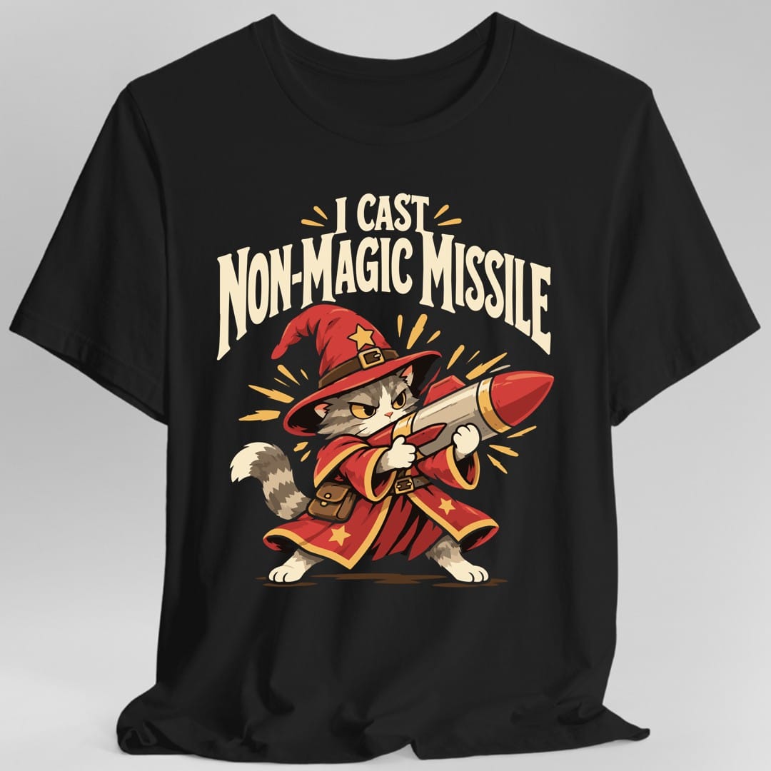 Black t-shirt. The design reads I CAST in cream capitals at the top and NON-MAGIC MISSILE in large arched cream capitals below it, with yellow spark marks around the words. Underneath, a grey and white cat with a stern expression stands in a red wizard hat and a long red robe trimmed in gold stars, a brown satchel at its belt, hoisting a large red tipped rocket across its body like a weapon.