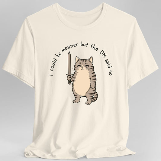Natural t-shirt. The words I could be meaner but the DM said no curve in a black handwritten arc across the top and down both sides. In the middle a chunky gray tabby cat stands upright on its hind legs with a flat, unimpressed expression and half closed eyes, holding a plain cream sword upright in one paw. Its chest and belly are pale cream, its back and tail striped. Simple black line cartoon style.
