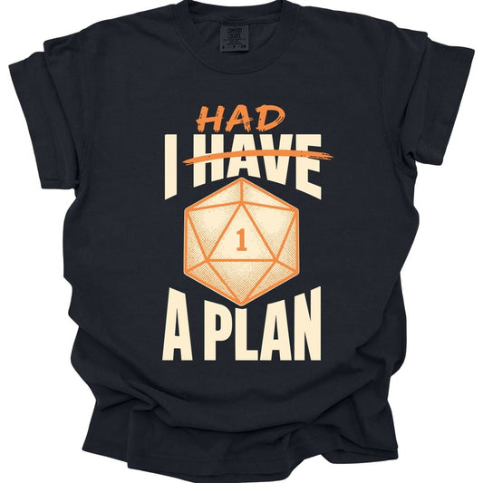Black t-shirt. Reads "I have" in large cream capitals with "have" struck through in orange and "Had" written above it in orange, so it reads "I had a plan", with "A plan" across the bottom. In the middle sits a large orange twenty-sided die showing 1.