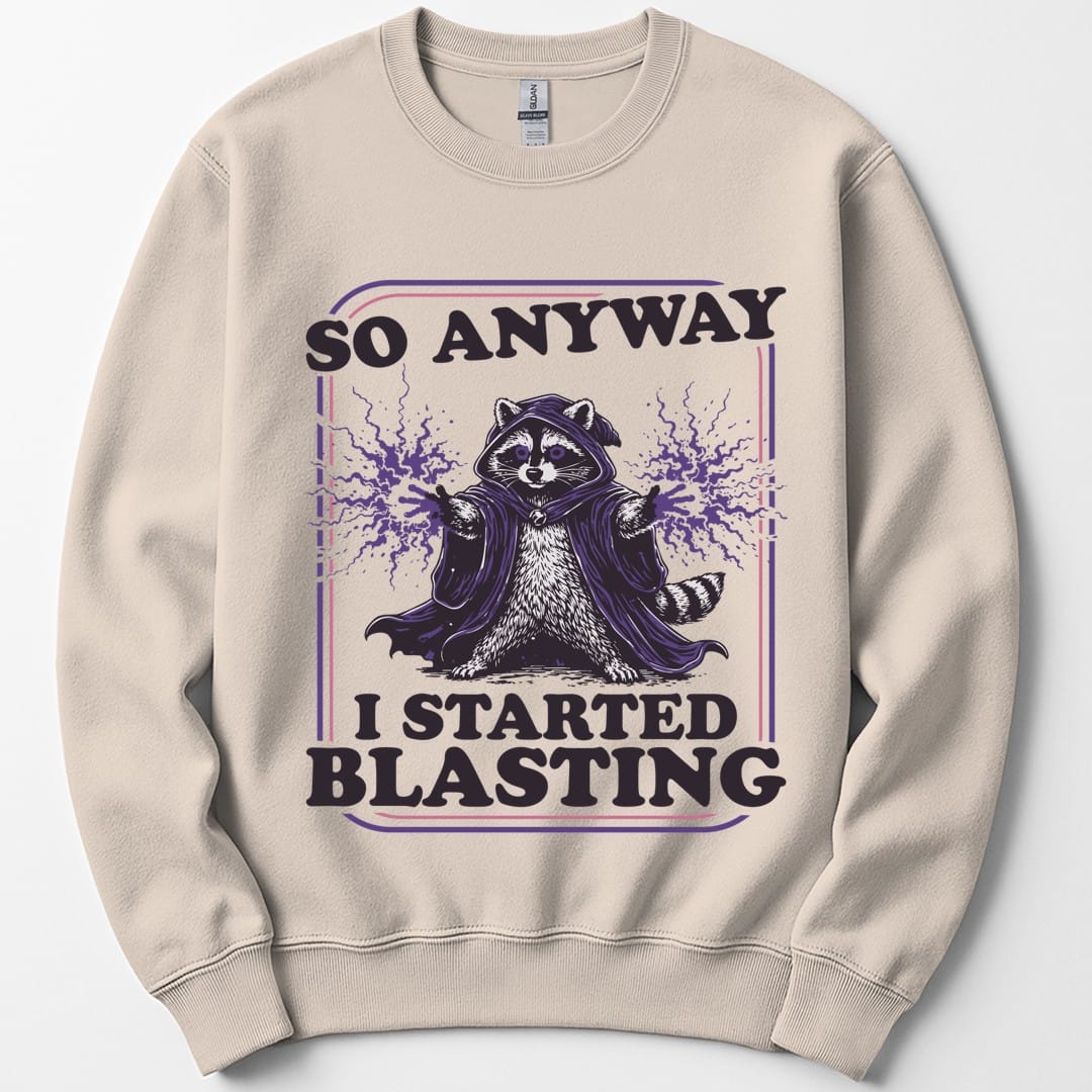 Sand sweatshirt. Reads "So anyway" across the top in dark capitals and "I started blasting" across the bottom. Between them a raccoon sits in a dark hooded cloak with both paws raised, purple magic crackling out from each one. Engraved linework in near-black and purple, no frame.