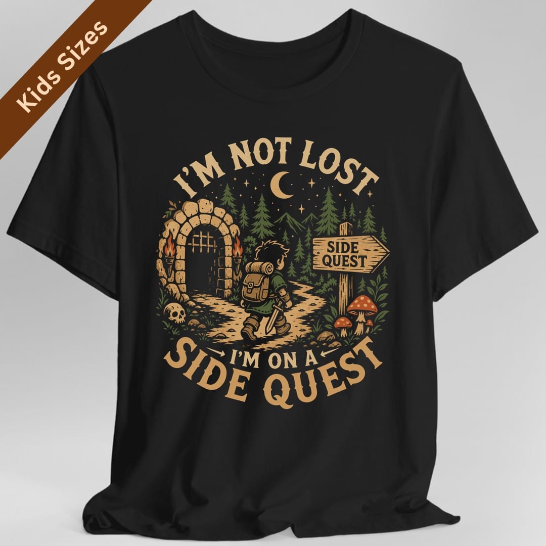 Black kids t-shirt. Reads "I'm not lost" curving across the top and "I'm on a side quest" across the bottom in gold capitals. Between them a hooded adventurer with a lantern walks a path away from a lit stone archway, past pines, red toadstools and a signpost reading "Side quest", under a crescent moon.