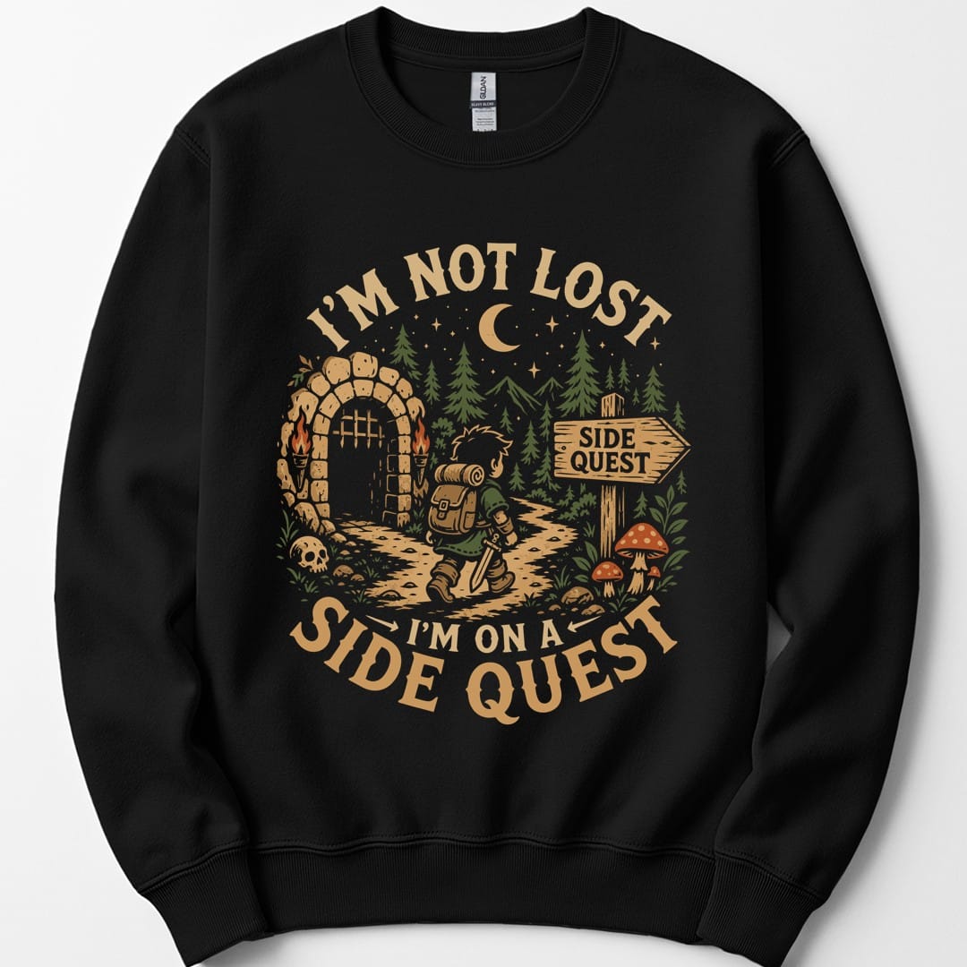 Black sweatshirt. Reads "I'm not lost" curving across the top and "I'm on a side quest" across the bottom in gold capitals. Between them a hooded adventurer with a lantern walks a path away from a lit stone archway, past pines, red toadstools and a signpost reading "Side quest", under a crescent moon.
