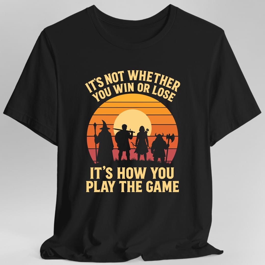 Black t-shirt. The design reads "It's not whether you win or lose" curved across the top and "It's how you play the game" in two big lines at the bottom, in pale gold letters. Between them, four adventurers stand in silhouette on grass: a wizard with a staff, a fighter shouldering a sword, an archer with a quiver, and a horned barbarian with an axe. Behind them is a pale moon inside a striped sunset going from orange down to deep red.