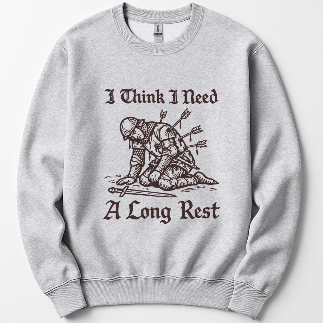 Ash sweatshirt. Reads "I Think I Need" across the top and "A Long Rest" across the bottom in ornate blackletter script. Between them a knight in chainmail and a domed helm kneels on all fours on the ground, stuck with four arrows and dripping, his sword fallen in front of him. Single color woodcut engraving in deep maroon brown.