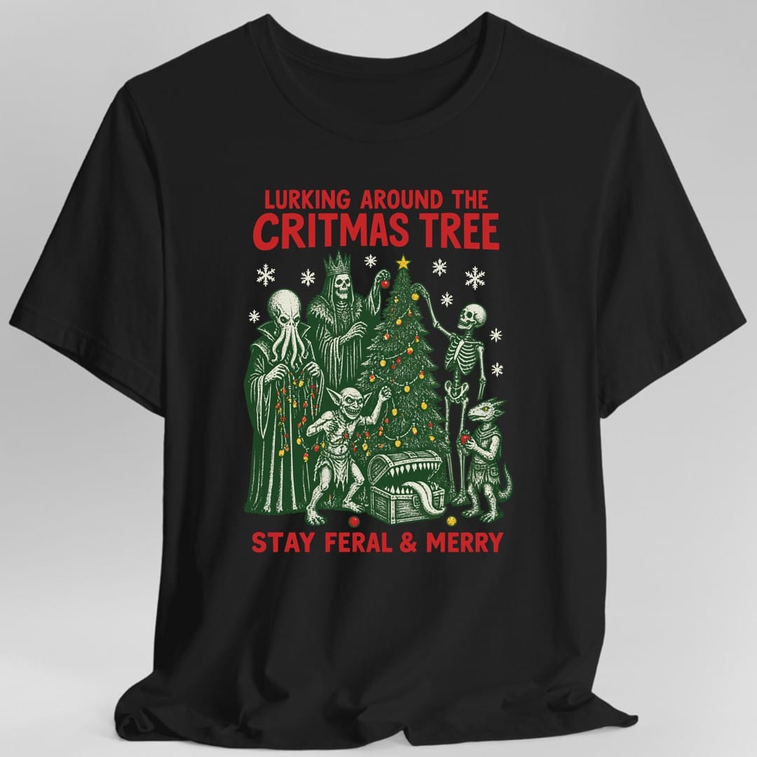 Black t-shirt. Reads "Lurking Around the Critmas Tree" in red across the top and "Stay Feral and Merry" in red across the bottom. Between them a decorated pine tree with a star on top, surrounded by five monsters hanging lights and ornaments: a tentacle faced mind flayer, a crowned skeletal lich, a skeleton, a grinning goblin and a small kobold. An open treasure chest sits at the base. Woodcut style art in deep green and bone white.