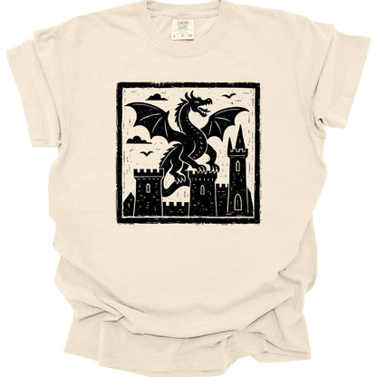 Ivory t-shirt. A square framed woodcut: a dragon with spread wings stands between two stone castle towers, with birds in the sky and hatched clouds behind. Heavy carved black line work filling the frame. No words.