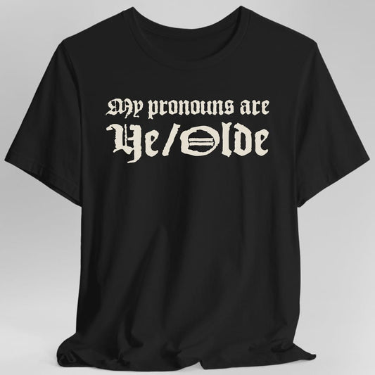Black t-shirt. The design reads My pronouns are Ye slash Olde in ornate blackletter type across two lines, the second line much larger than the first. There is no other imagery. Printed as a single block of text sitting high on the chest.