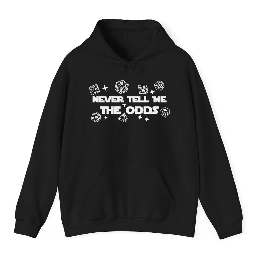 Black hoodie. Reads "Never tell me" over "The odds" in bold white capitals across the middle. Polyhedral dice of every shape float loose around the words, drawn as simple white outlines, with a few four-pointed sparkles between them.