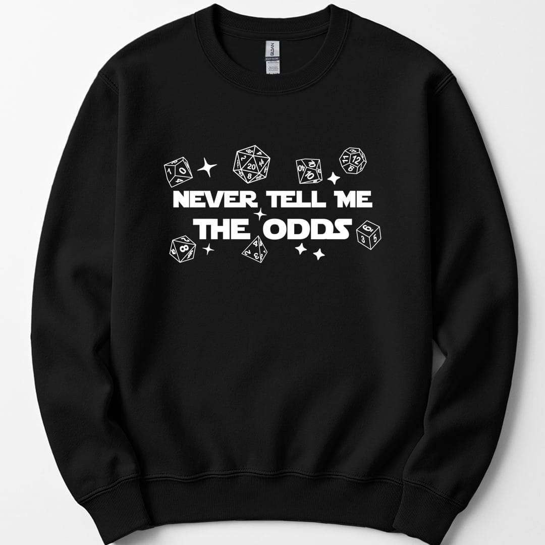 Black sweatshirt. Reads "Never tell me" over "The odds" in bold white capitals across the middle. Polyhedral dice of every shape float loose around the words, drawn as simple white outlines, with a few four-pointed sparkles between them.