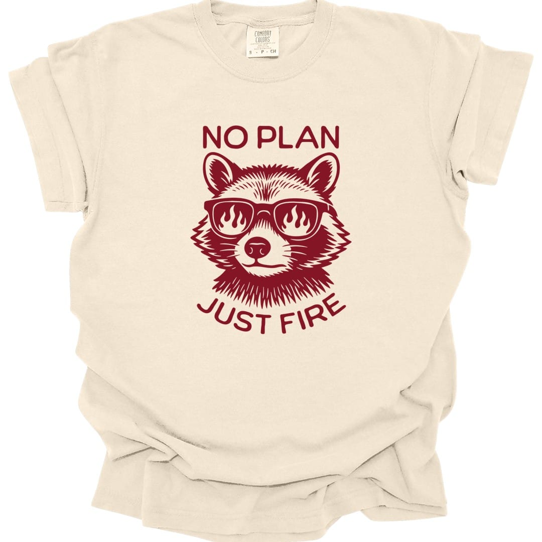 Ivory t-shirt. Reads "No plan" across the top and "Just fire" across the bottom in dark red capitals. Between them a raccoon faces forward wearing sunglasses with flames reflected in the lenses. Drawn in engraved lines, all in a single deep red.