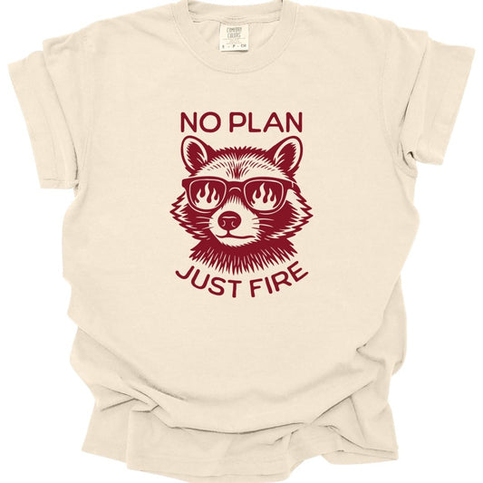 Ivory t-shirt. Reads "No plan" across the top and "Just fire" across the bottom in dark red capitals. Between them a raccoon faces forward wearing sunglasses with flames reflected in the lenses. Drawn in engraved lines, all in a single deep red.