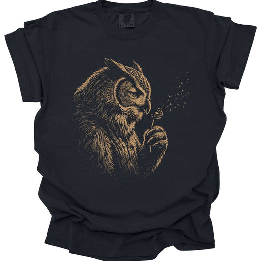 Black t-shirt. An owlbear sits in profile, head bowed, blowing the seeds off a dandelion clock held in one claw, with the seeds drifting away to the right. Drawn in soft faded gold line work, almost ghostly against the shirt. No words.