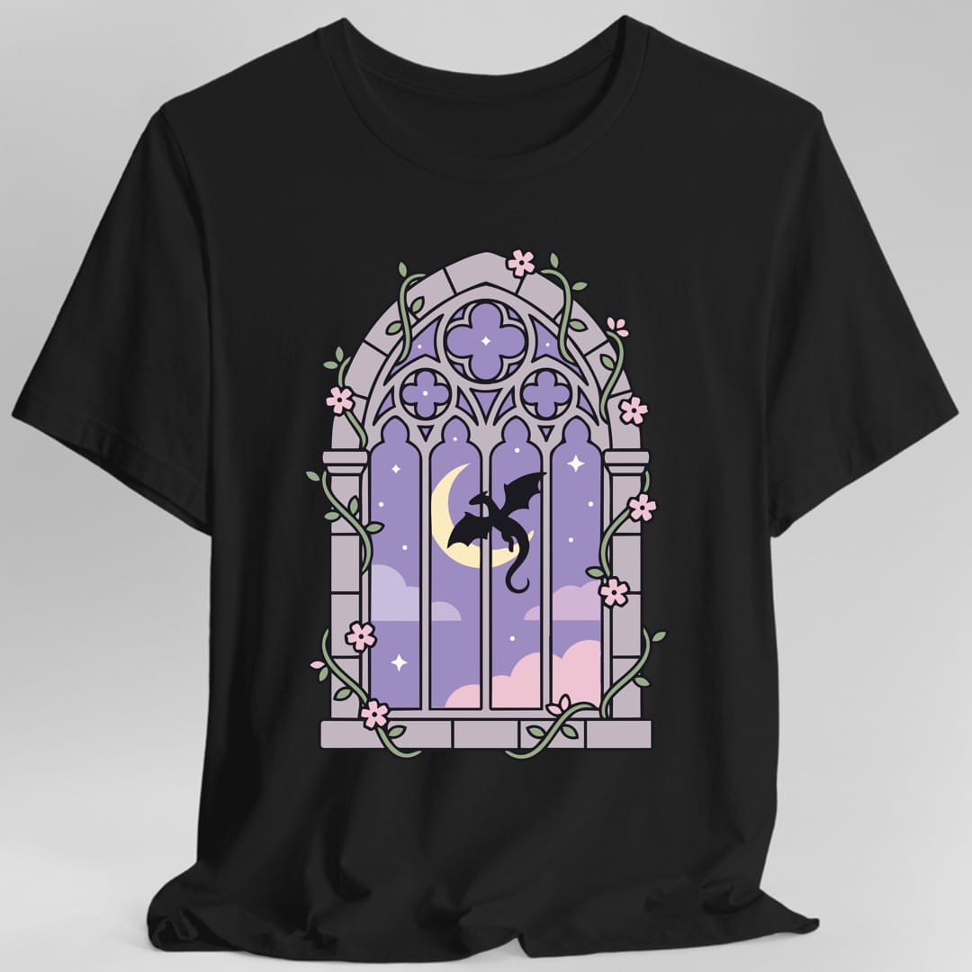 Black t-shirt. A tall gothic cathedral window in pale lilac and lavender, with stone tracery and a quatrefoil at the top. Inside, a small black dragon flies in front of a crescent moon and pink clouds. Green vines and pink blossoms twine around the frame. No words.