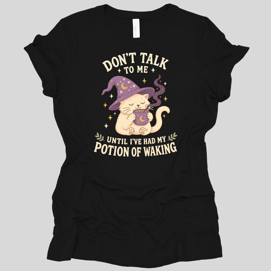 Black women's t-shirt. Reads "Don't talk" across the top with "to me" beneath, and "Until I've had my" and "Potion of waking" across the bottom in cream capitals. Between them a cream cat in a purple starry wizard hat holds a steaming mug in both paws, eyes closed.
