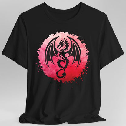 Black t-shirt. A dragon in silhouette coils in a circle with its wings spread and tail curling round, set against a rough circular splash of watercolour that runs from pink to deep red, with paint specks flicked around the edges. No words.
