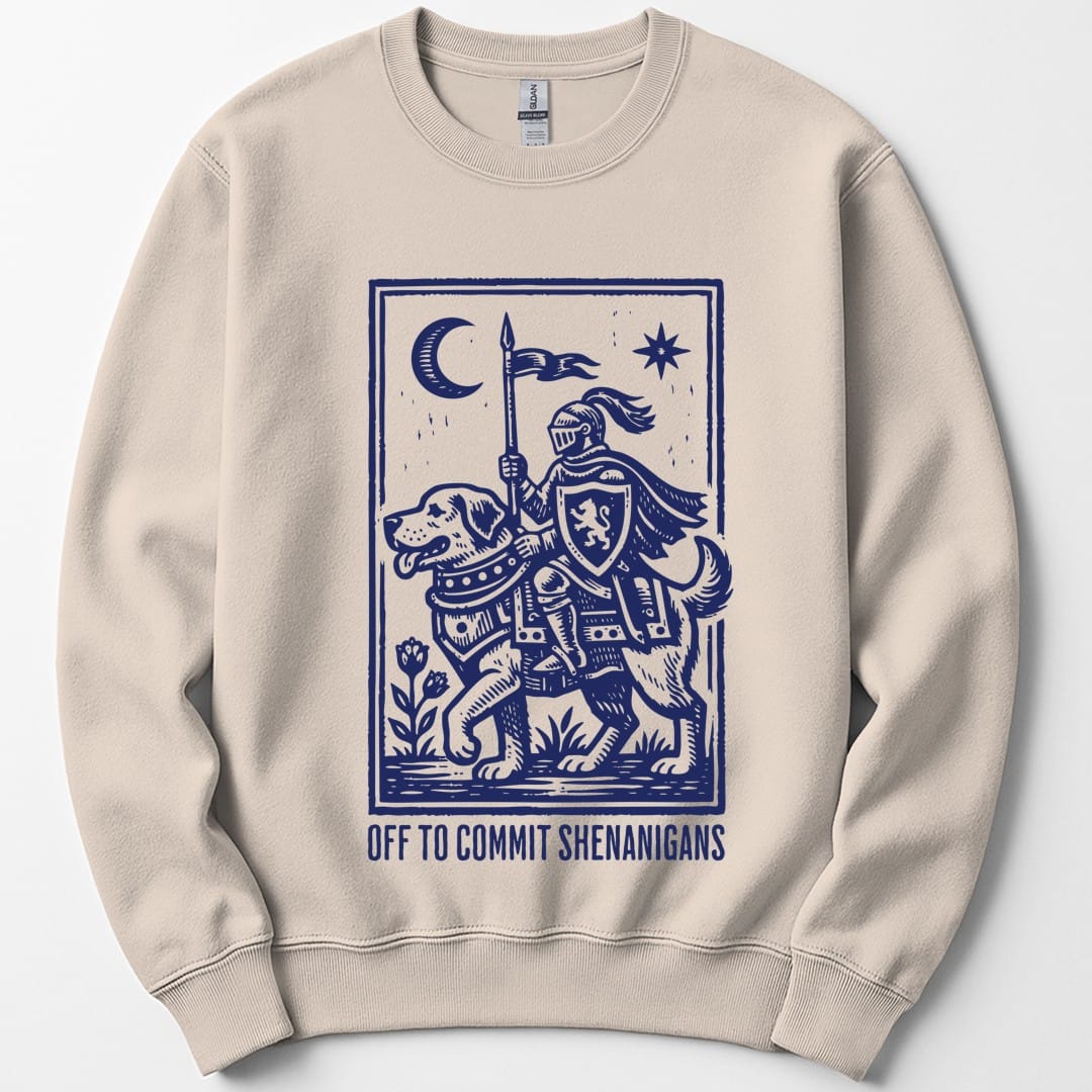 Sand sweatshirt. A knight in full armor rides a large hound like a horse, carrying a lance with a pennant, under a crescent moon and a star, all inside a thin ruled border. Underneath, "Off to commit shenanigans" in spaced capitals. Medieval woodcut style, all in one deep blue.