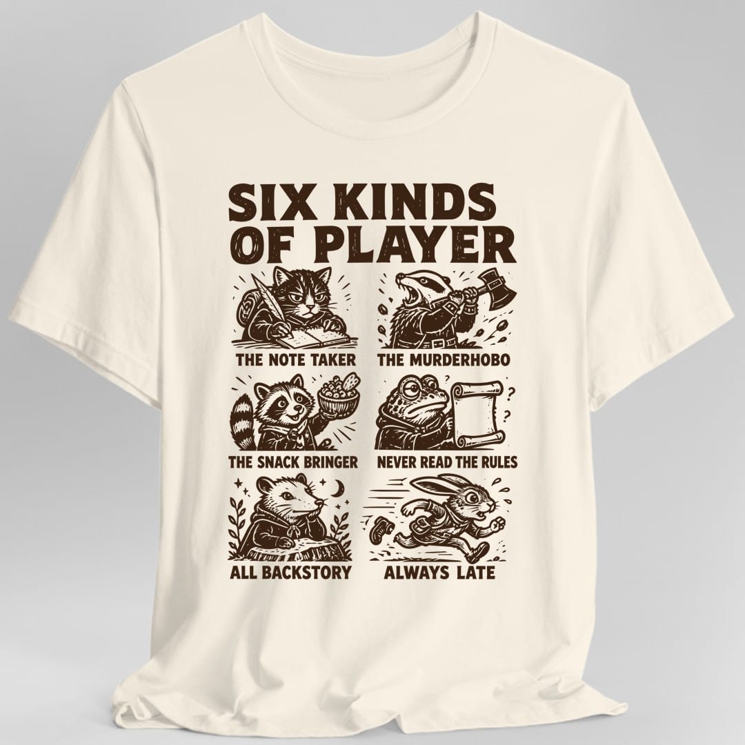 Natural t-shirt. The design reads SIX KINDS OF PLAYER in heavy dark brown capitals across the top, above a grid of six woodcut style animals, each labeled underneath. A cat writing with a quill, THE NOTE TAKER. A badger swinging an axe, THE MURDERHOBO. A raccoon holding a bowl of snacks, THE SNACK BRINGER. A frog squinting at a scroll, NEVER READ THE RULES. An opossum lounging, ALL BACKSTORY. A rabbit running, ALWAYS LATE.