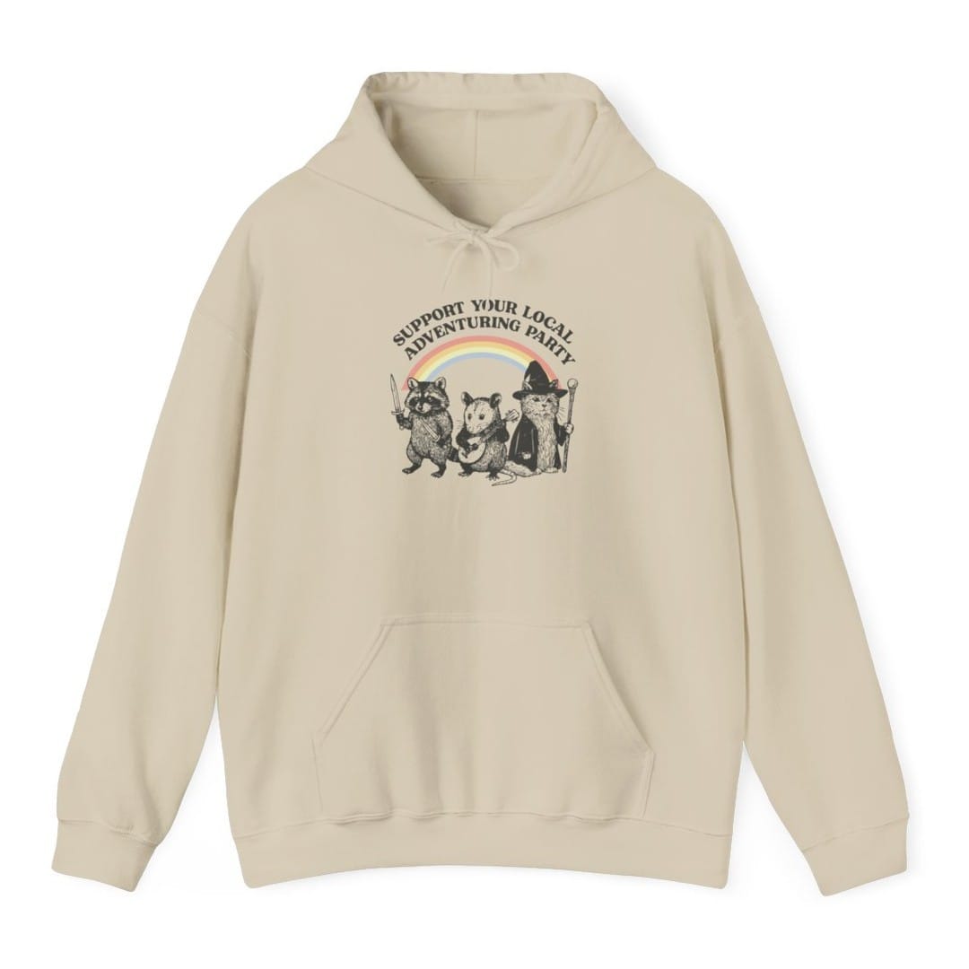 Sand hoodie. Reads "Support your local adventuring party" curving across the top in dark capitals. Below, three animals stand in a row: a raccoon holding a sword, an opossum with a dagger, and a cat in a pointed wizard hat with a staff. A soft pastel rainbow arcs behind them. Engraved linework over flat pastel color.