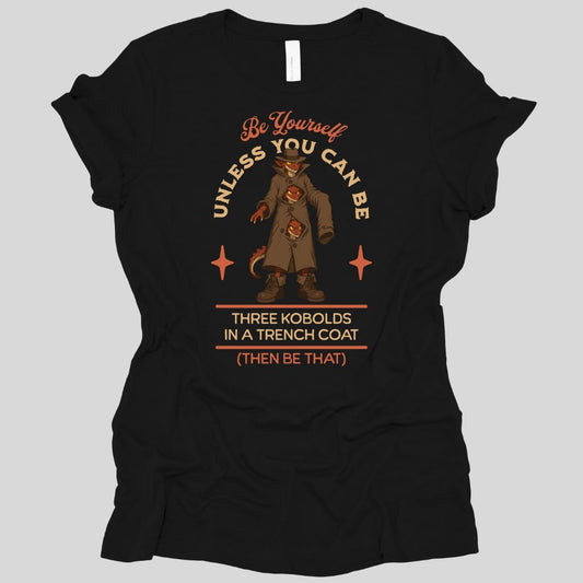 Black women's t-shirt. The design reads "Be yourself" in script at the top, then "unless you can be" curving around the picture, then "Three kobolds in a trench coat" on two lines below, then "(then be that)" at the bottom. In the middle, three small red kobolds are stacked inside one long tan trench coat and a fedora, the top one grinning out from under the hat brim and the other two peering through gaps between the buttons, with a tail poking out of the hem. Bold cartoon art in tan, rust and dark red.