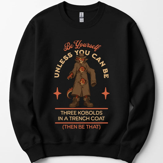 Black sweatshirt. The design reads "Be yourself" in script at the top, then "unless you can be" curving around the picture, then "Three kobolds in a trench coat" on two lines below, then "(then be that)" at the bottom. In the middle, three small red kobolds are stacked inside one long tan trench coat and a fedora, the top one grinning out from under the hat brim and the other two peering through gaps between the buttons, with a tail poking out of the hem. Bold cartoon art in tan, rust and dark red.