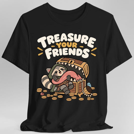 Black t-shirt. The design reads "Treasure Your Friends" in chunky rounded cream lettering with "Your" in gold across the top. Below, a cute cartoon raccoon in a green hooded cloak and belt sits inside an open wooden treasure chest that has teeth and a long pink tongue, a mimic monster, and hugs the tongue happily. Gold coins, a blue gem, a red gem and a goblet with a pearl necklace spill around the chest. Cute kawaii cartoon style with bold outlines.