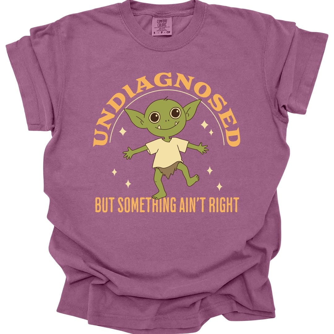The same Undiagnosed But Something Ain't Right goblin design, on a berry t-shirt.