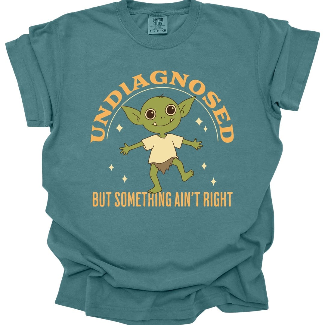 The same Undiagnosed But Something Ain't Right goblin design, on a blue spruce t-shirt.