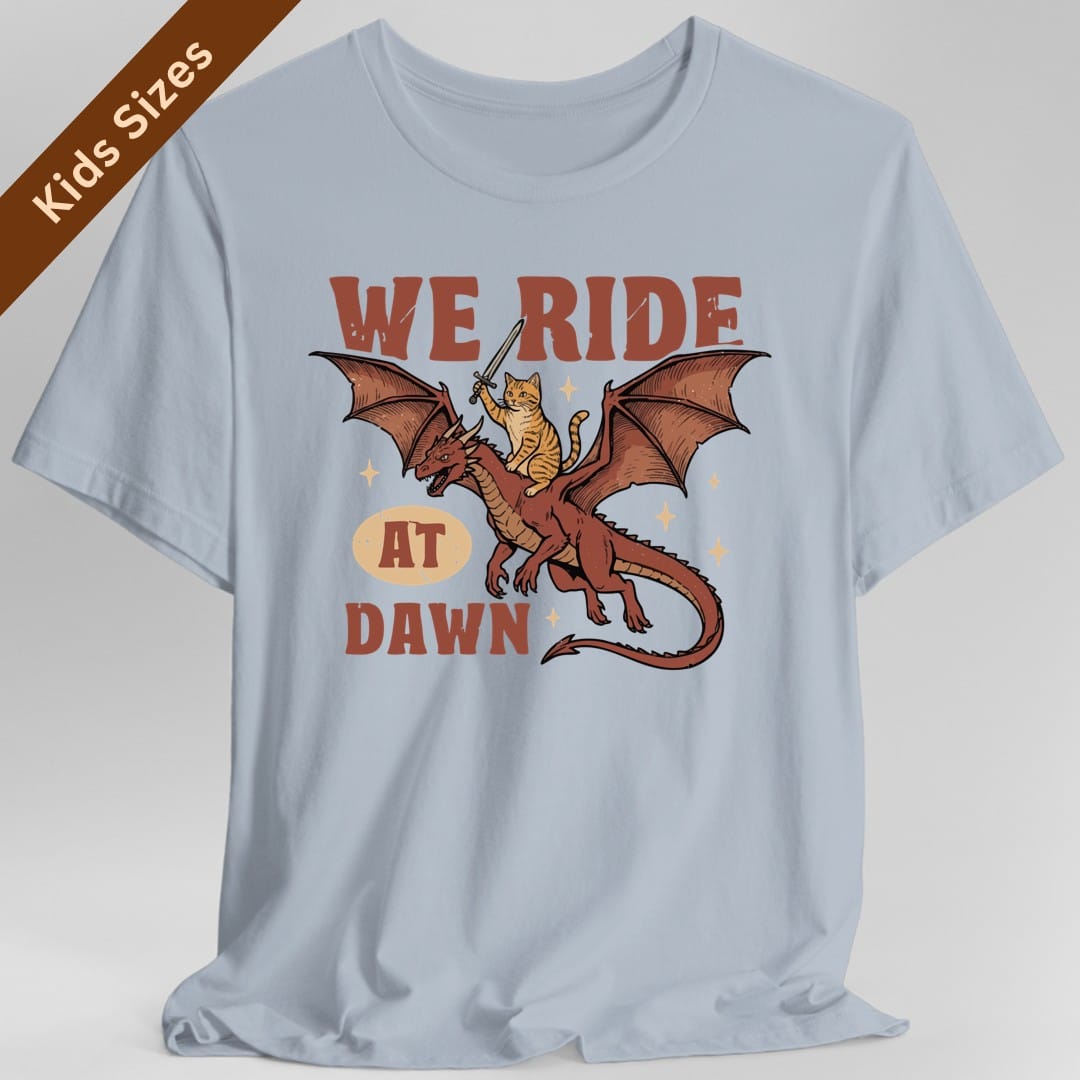 The same We Ride At Dawn dragon cat design, on a light blue kids t-shirt.