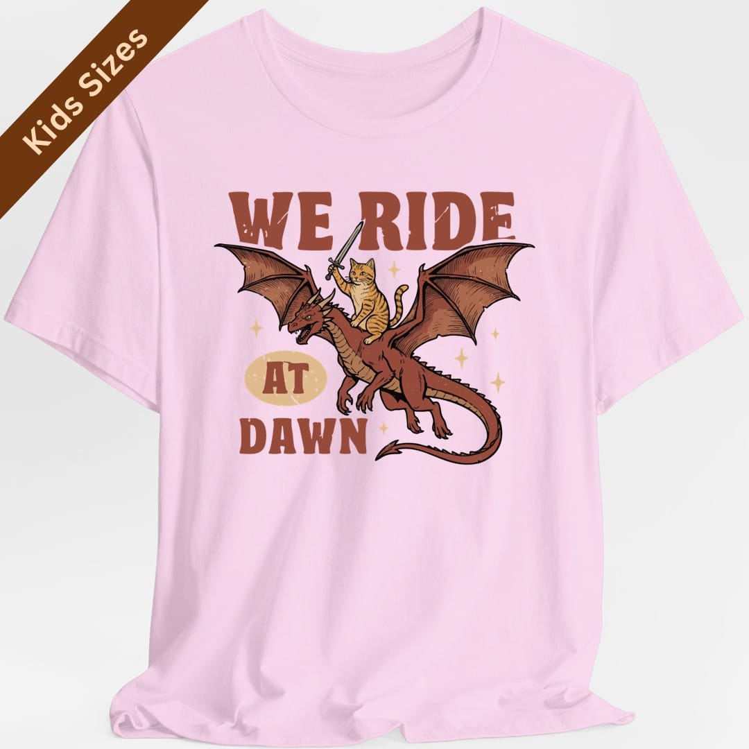 The same We Ride At Dawn dragon cat design, on a light pink kids t-shirt.