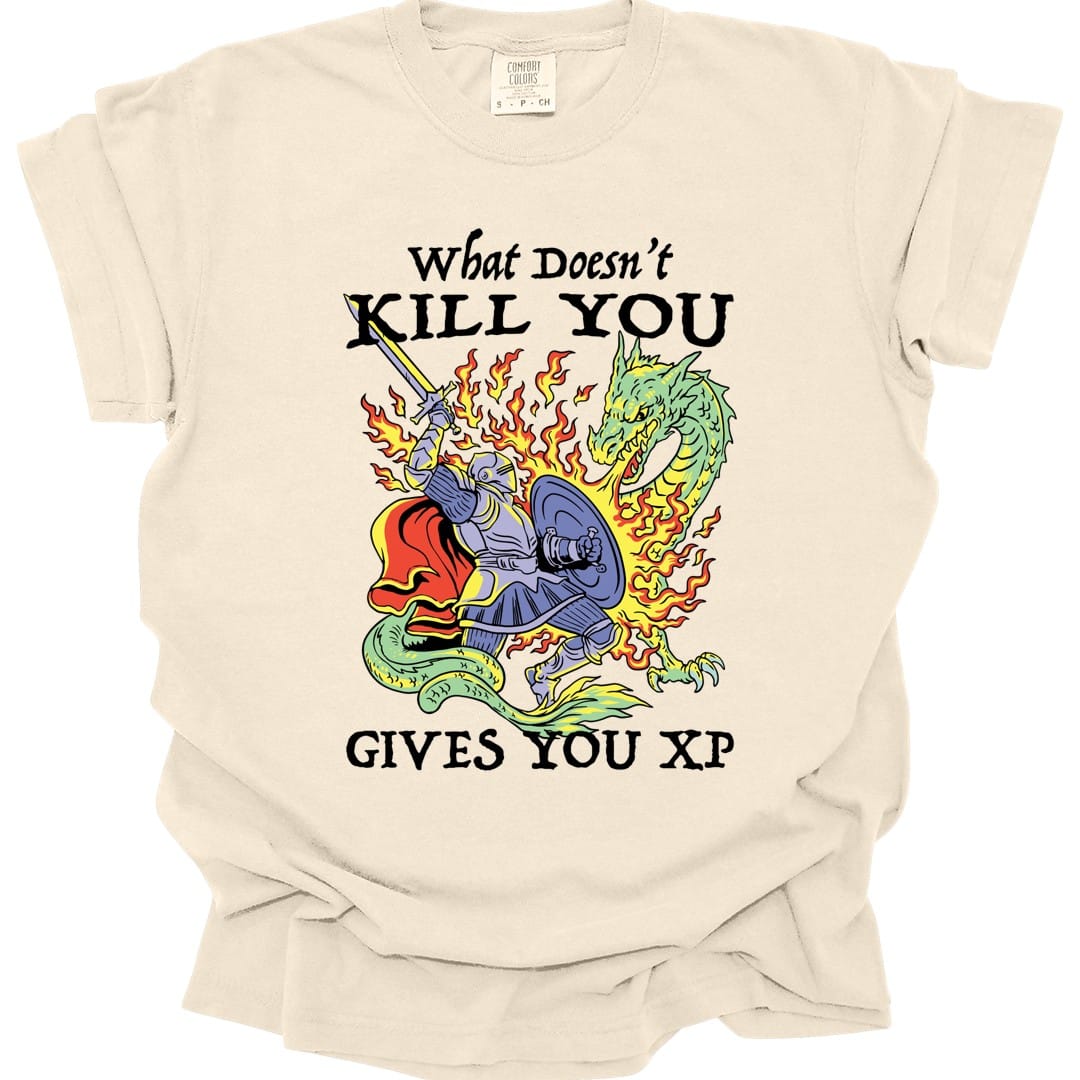 Ivory t-shirt. Reads "What doesn't" in script above "Kill you" in bold capitals, with "Gives you XP" across the bottom. Between them a knight in blue armor drives a sword into a green dragon, flames bursting around them. Bright cartoon style in blue, green, yellow and red.